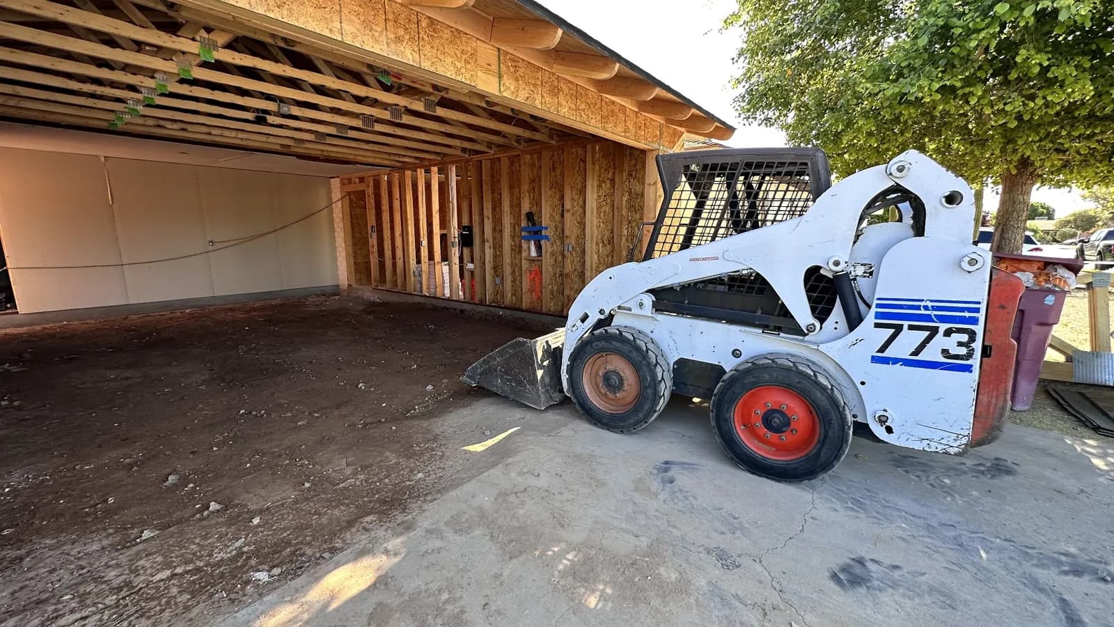 Skid steer on a new slab next to fresh framing on a Masizo job site