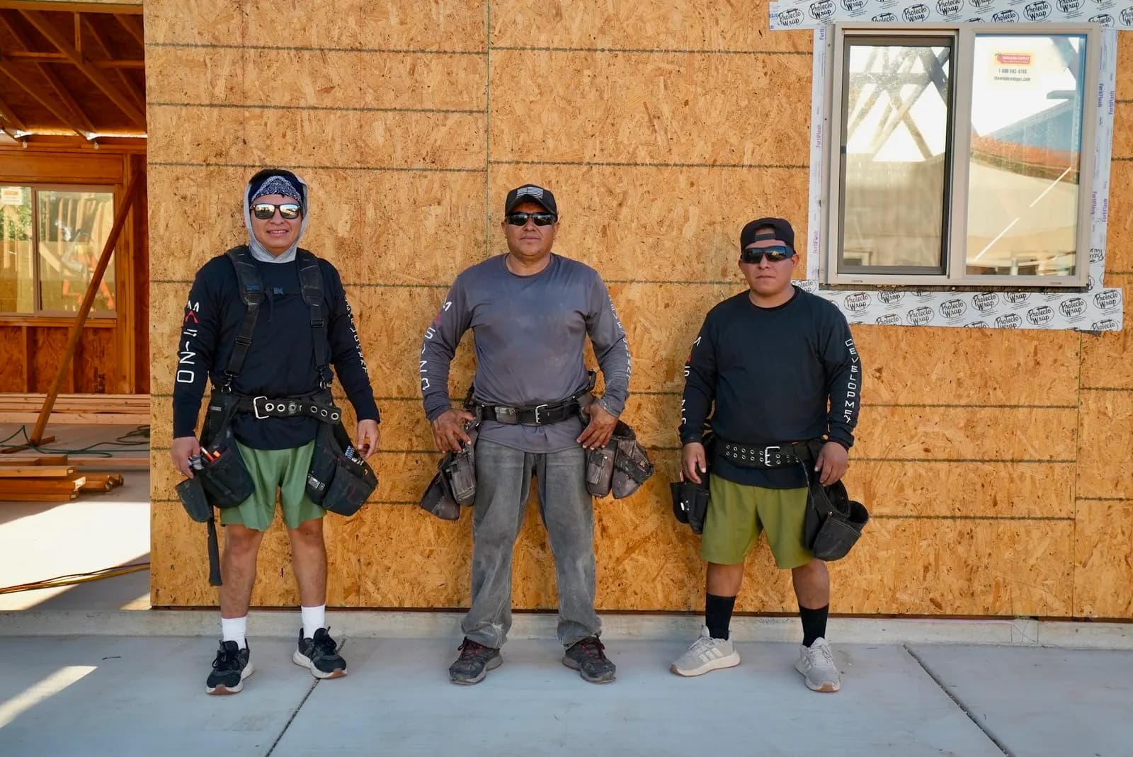 Three Masizo crew members in front of a sheathed wall on a new build