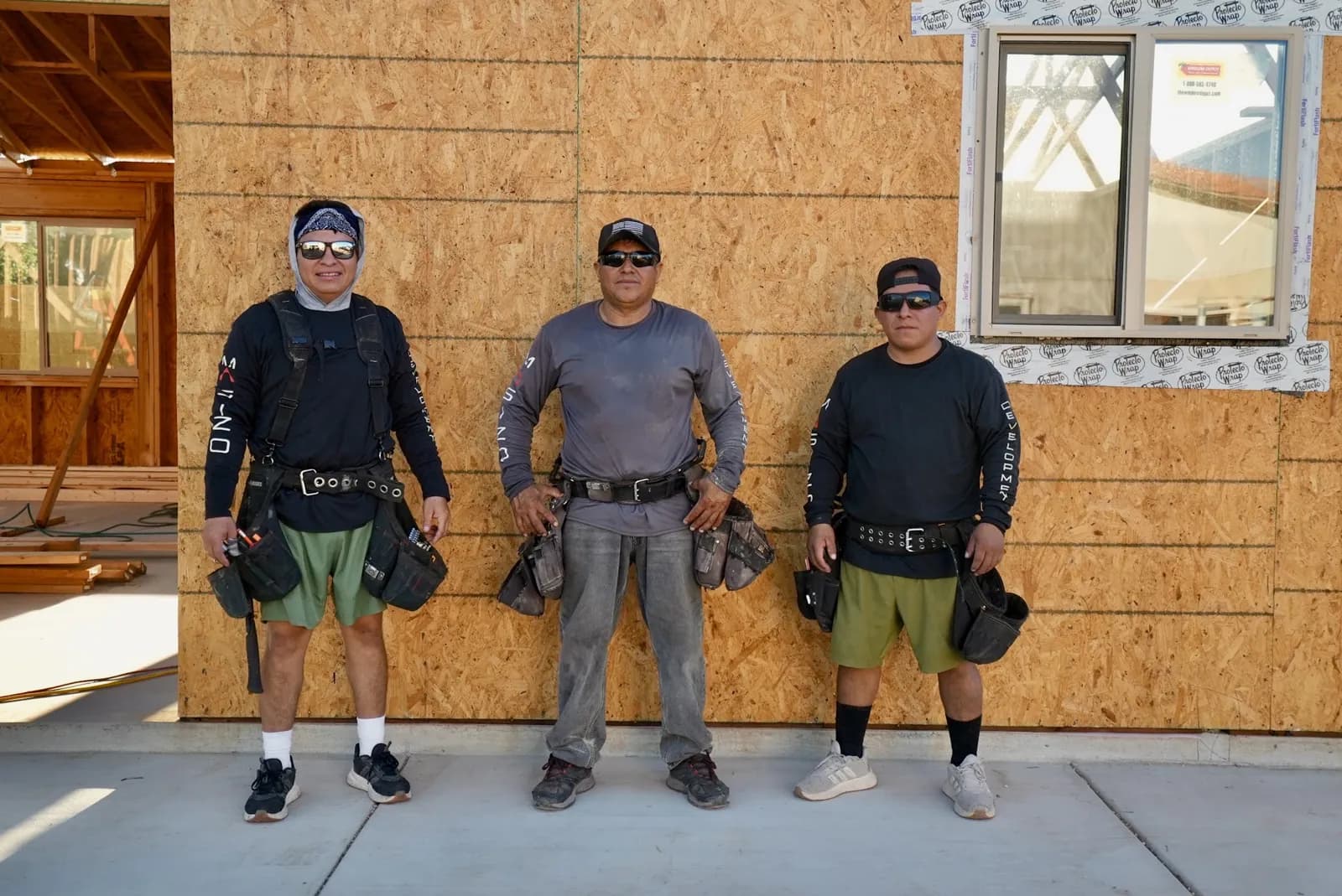 Three Masizo crew members in front of a sheathed wall on a new build