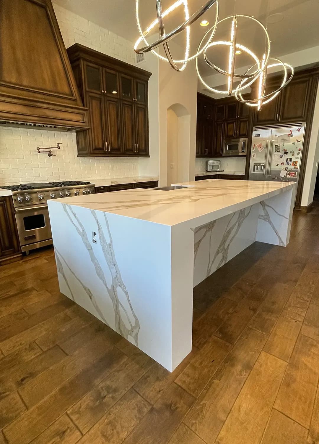 Marble-look waterfall island under round pendant lights in a Masizo kitchen