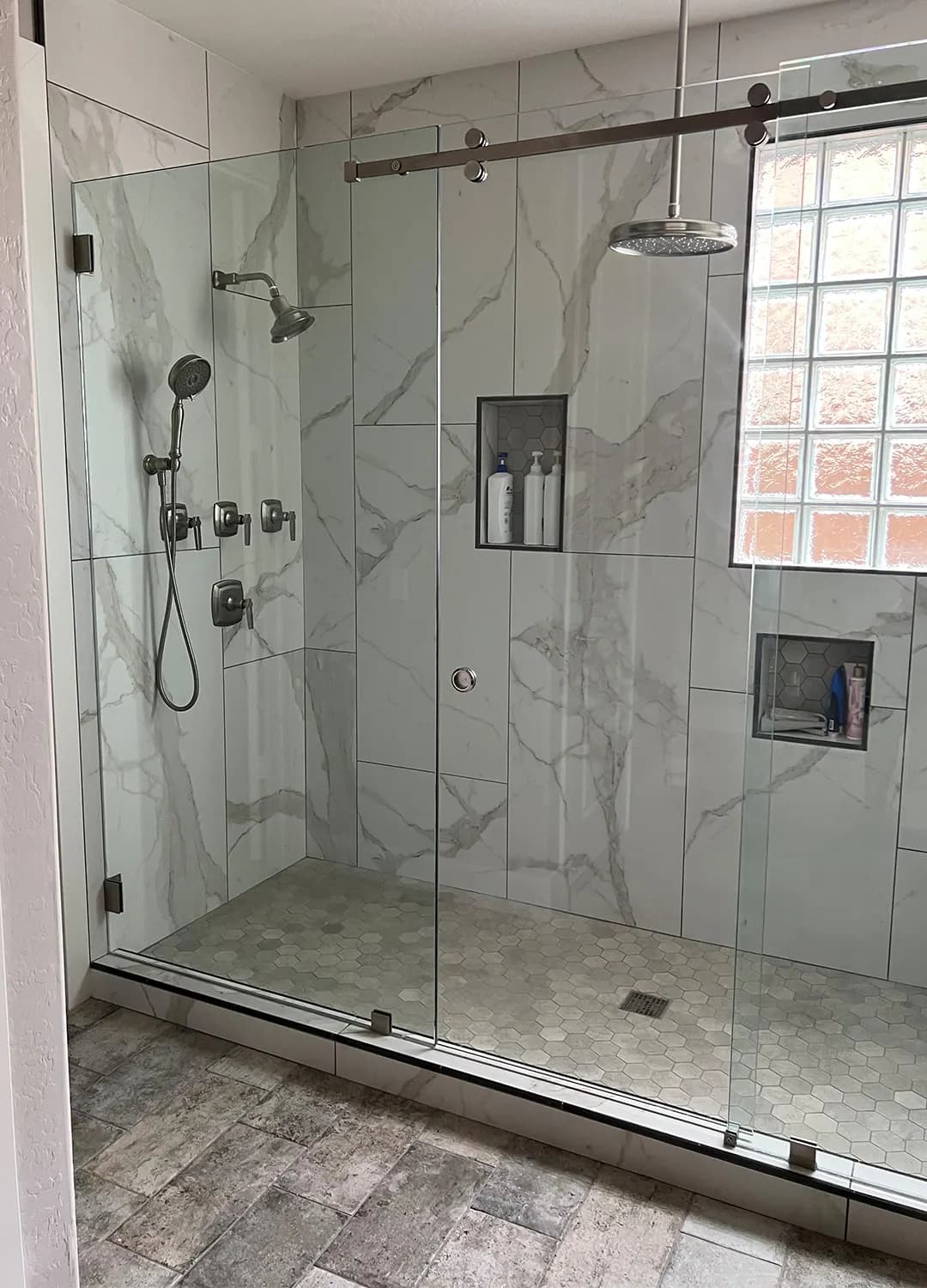 Walk-in shower with marble-look tile, two niches and a glass door on a Masizo job