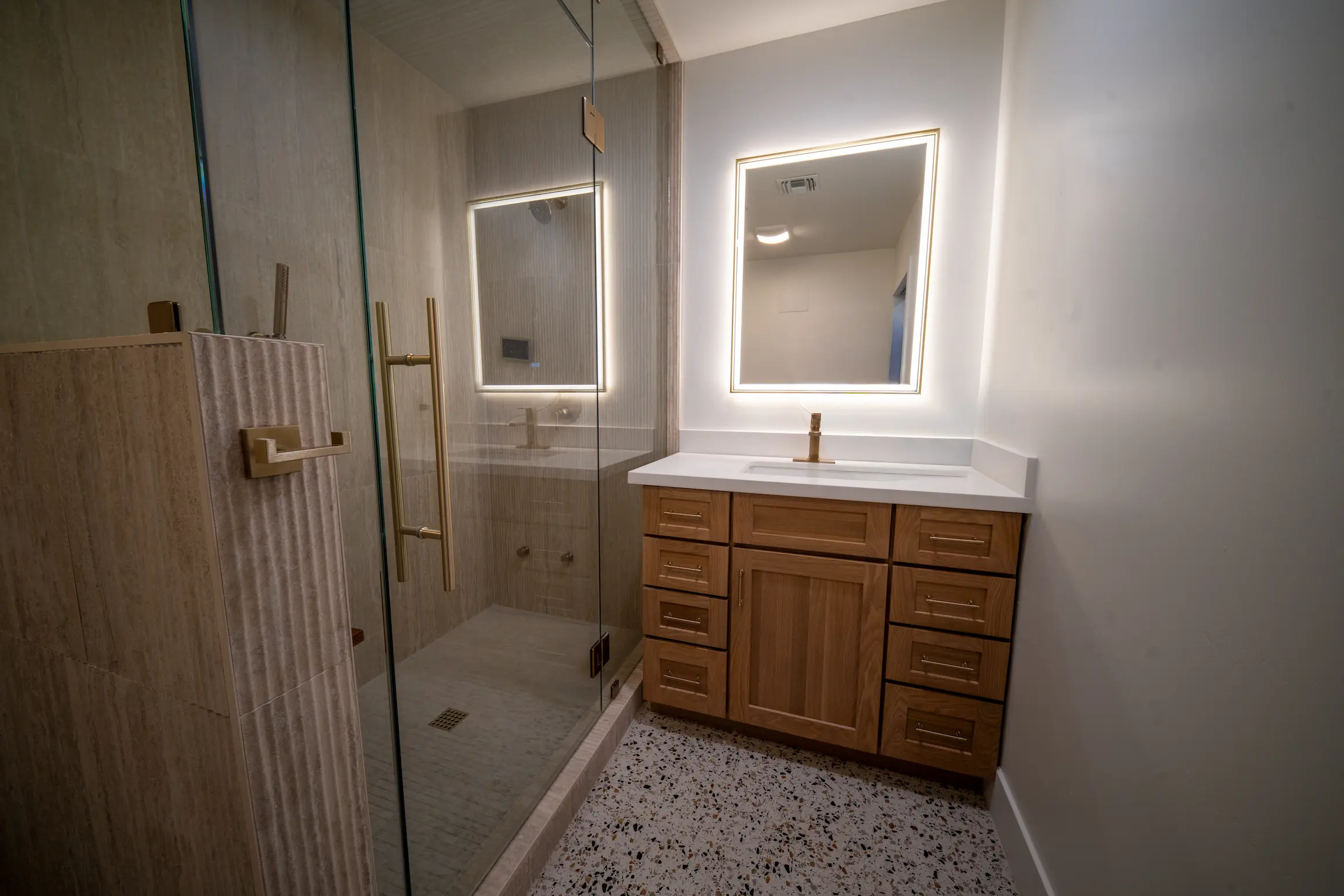 Bathroom remodel with a glass shower, wood vanity and lighted mirrors
