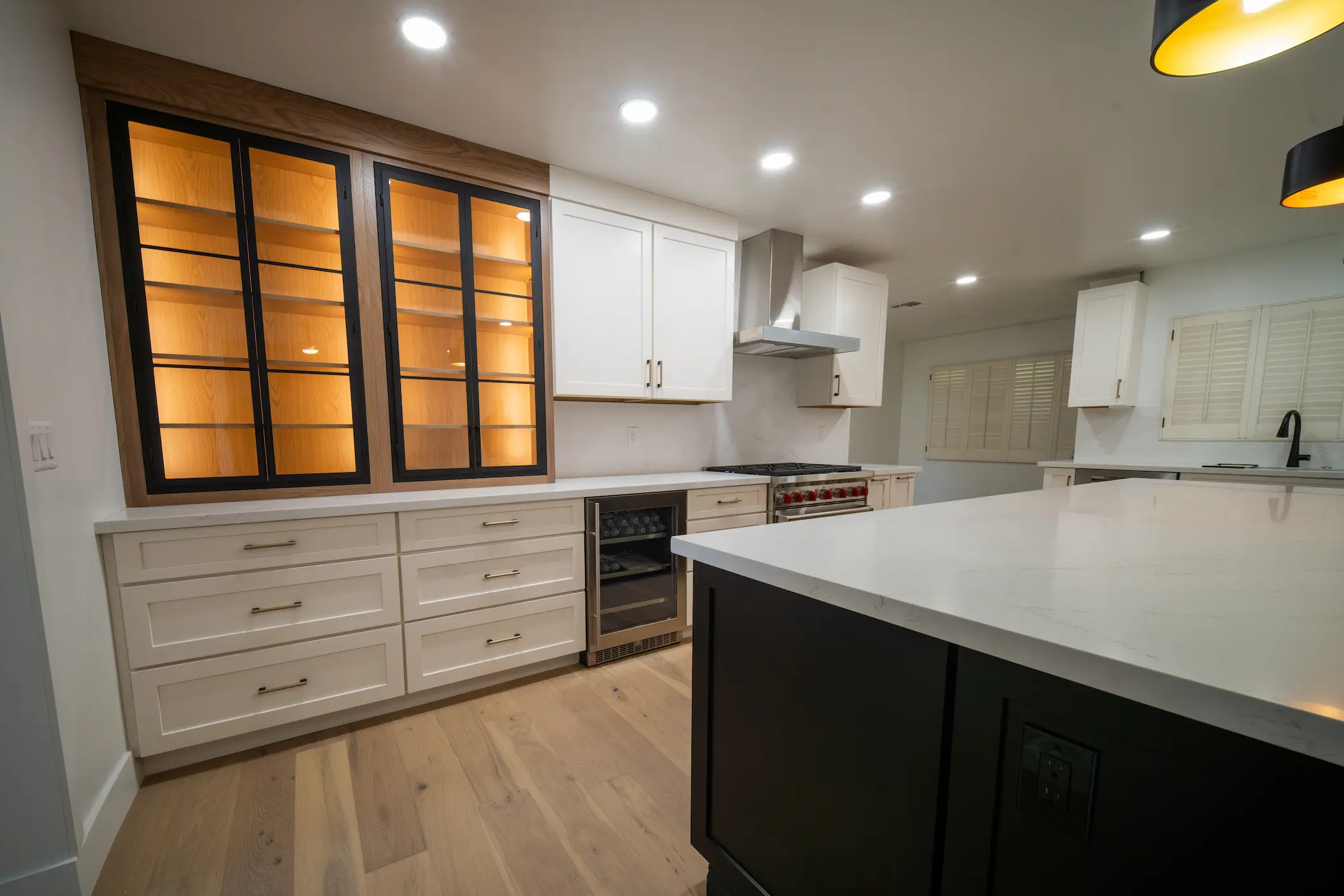 White kitchen cabinets with lit glass-front uppers and a dark island